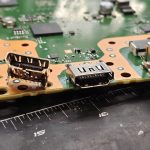 Broken HDMI port next to its new replacement on a PS5 motherboard at Device Hero in Manor, TX