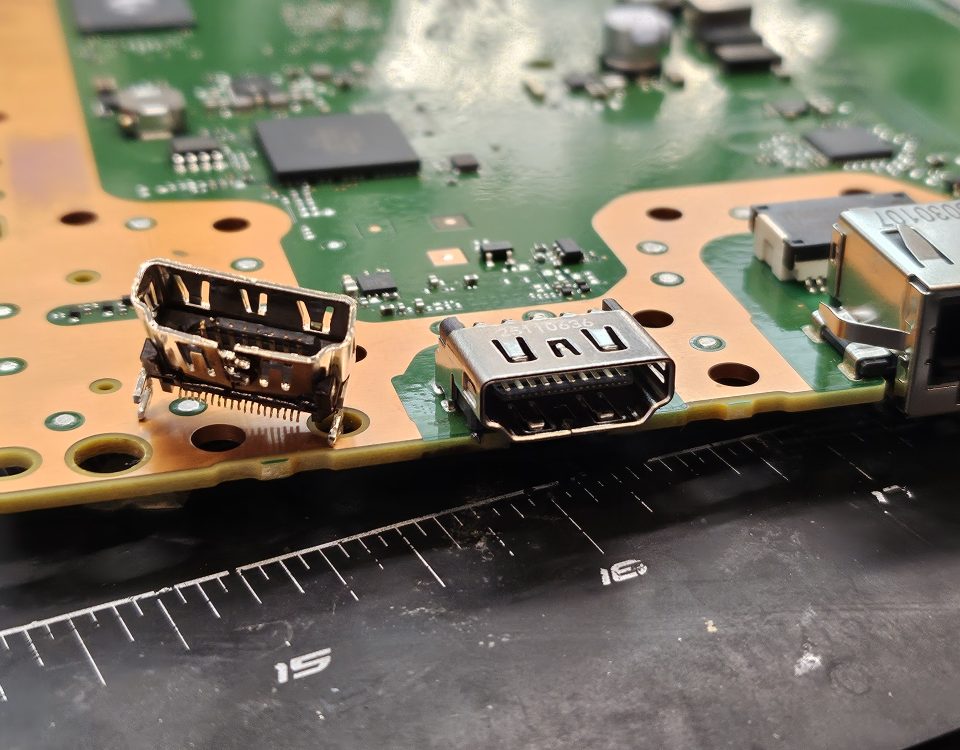 Broken HDMI port next to its new replacement on a PS5 motherboard at Device Hero in Manor, TX